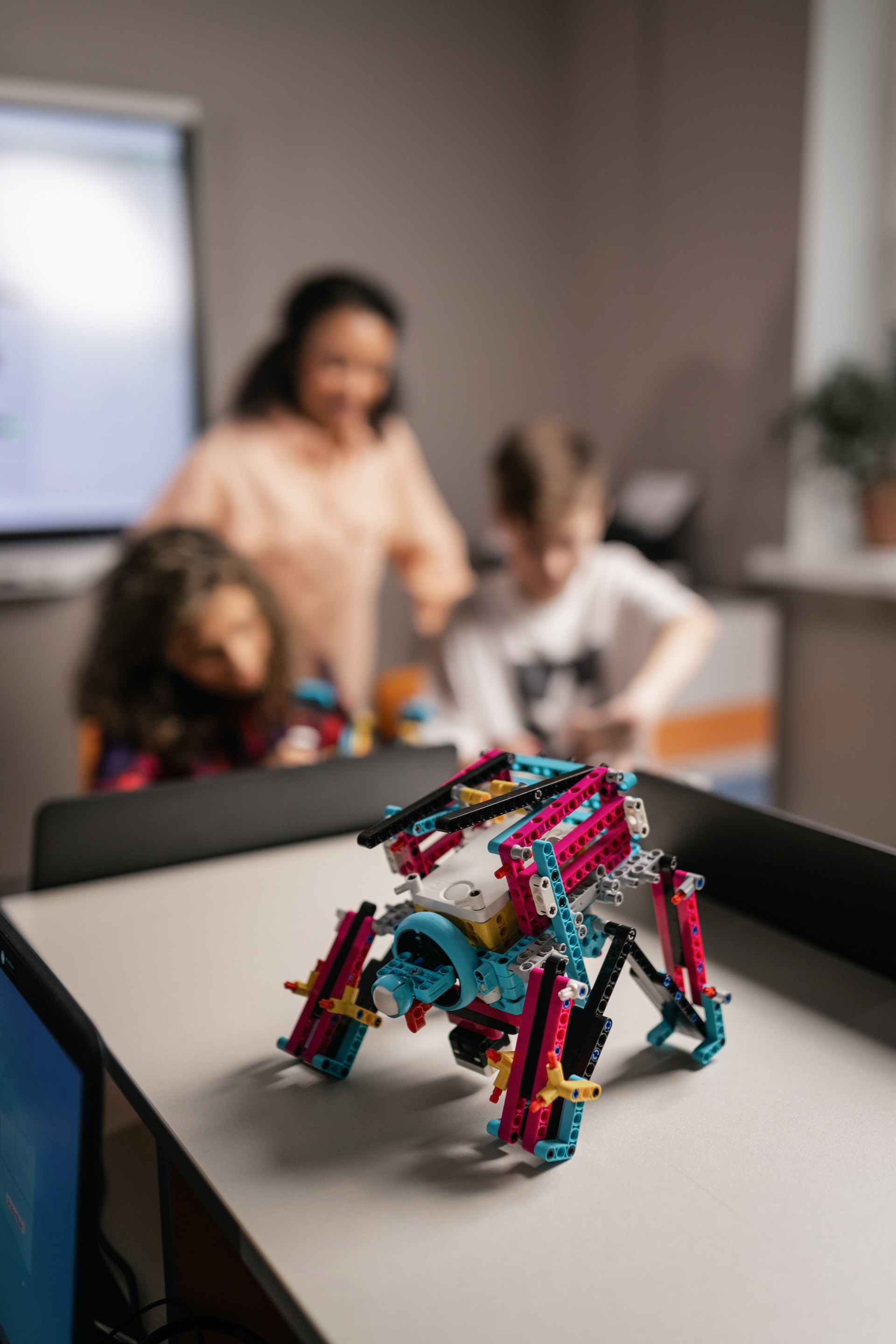 a small robot in the foreground and a teacher and students working in the background